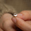 a person&#39;s hand holding a tiny silver ring