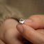 a person&#39;s hand holding a tiny silver ring