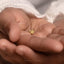 A person's hand holding a small gold-colored charm with the text "DAD" engraved on it.