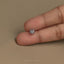 A person's thumb is holding a small, delicate silver earring.