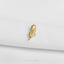 A small gold leaf-shaped pin is resting on a white fabric surface.