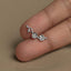 A close-up image of a person's fingers holding a small silver earring with a floral design.