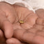 A close-up image of a person's hand holding a small gold-colored object, possibly a piece of jewelry.