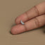 A person's left index finger is holding a small silver earring against a beige background.