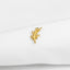 A small gold leaf pin is resting on a white fabric surface.