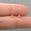 A pair of gold-colored triangle-shaped stud earrings being held between two fingers.