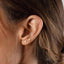 A close-up of a person's ear with three small heart-shaped earrings attached.