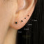 a close-up of a person's ear with several small black earrings, each with a different size indicated in millimeters.
