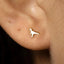 A close-up view of a person's ear with a small, white earring shaped like a dinosaur.