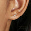 A close-up of a person's ear with a small gold earring featuring a row of small diamonds.