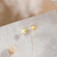 A pair of gold earrings with smiley faces on them, placed on a white surface against a blurred background.