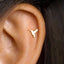 A close-up view of a person's ear, showing a small gold hummingbird-shaped earring inserted into the earlobe.