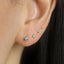 A close-up of a person's ear with a row of small turquoise-colored earrings attached to the earlobe.