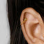 A close-up view of a person's ear with a gold-colored earring attached to the side of the ear.