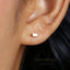 A close-up view of a person's ear with a small, square-shaped earring in it.