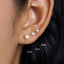 A close-up of a person's ear with three pearl earrings of different sizes, labeled with their respective measurements.