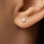 A close-up view of a person's ear, showing a small silver earring with a flower design.
