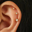 A close-up of a person's ear with three small gold earrings attached.