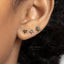 A close-up of a person's ear with three small, black diamond-encrusted earrings.