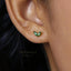 A close-up of a person's ear wearing a small green leaf-shaped earring.