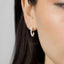 A close-up of a person's ear wearing a small hoop earring with white pearls.