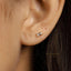 A close-up of a person's ear with a small, rectangular-shaped earring attached.