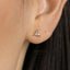 A close-up of a person's ear with a small, triangular-shaped earring featuring a clear gemstone.