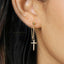 A close-up view of a person's ear wearing a gold cross-shaped earring with a dangling chain.