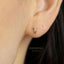 A close-up of a person's ear wearing a small gold earring with a diamond.