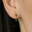 A close-up of a person's ear wearing a pair of gold earrings with green gemstones.