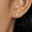 A close-up of a person's ear wearing a small gold cross earring.