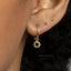 A close-up view of a person's ear wearing a gold-colored earring with a small sun-shaped charm hanging from it.