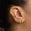 A close-up of a person's ear adorned with multiple green gemstone earrings.