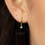 A close-up view of a person's ear adorned with a gold hoop earring featuring a blue gemstone.
