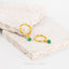 A pair of gold earrings with green gemstones, resting on a white surface.