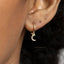 A close-up view of a person's ear with a small gold earring featuring a crescent moon charm hanging from it.