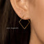 a close-up view of a person's ear wearing a pair of gold-colored diamond-shaped earrings.