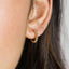 A close-up view of a person's ear with a gold hoop earring featuring a row of small, round beads.