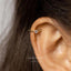 A close-up of a person's ear with a gold earring featuring a small diamond in the center.