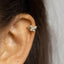 A close-up view of a person's ear with a delicate gold-colored earring featuring a small, intricately designed butterfly-shaped gemstone.