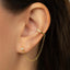 A close-up view of a person's ear adorned with a gold-colored earring and a matching gold-colored ear cuff.