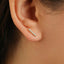 A close-up view of a person's ear, showing a delicate gold earring with a row of small diamonds.