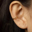 A close-up view of a person's ear with a gold-colored earring or ear cuff.