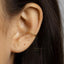 A close-up view of a person's ear with a gold-colored earring inserted, showing the earlobe and the earring itself.