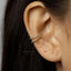 A close-up view of a person's ear adorned with a gold-colored ear cuff featuring a diamond-encrusted design.