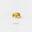 A gold-colored ring with a curved band is shown against a white background.