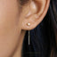 A close-up of a person's ear wearing a pair of gold earrings with a small square-shaped accent piece.