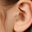 A close-up of a person's ear with a small, delicate earring featuring three small diamonds.
