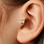 A close-up of a person's ear with a delicate earring featuring three opal stones.