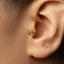 A close-up view of a person's ear, showing a small gold-colored earring with a rose design.